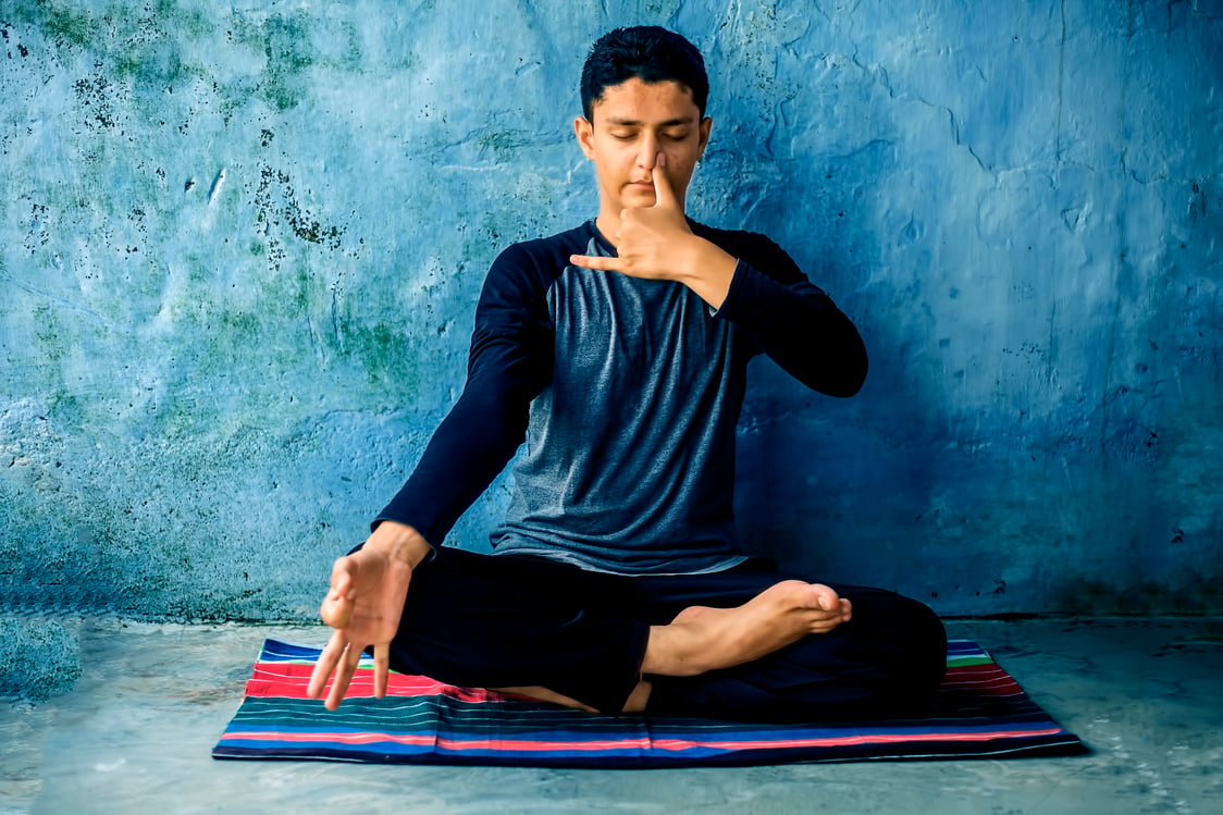 Portrait shot of the young man doing pranayama or pranayam or breath control yoga on a colorful mat with wearing black attire.